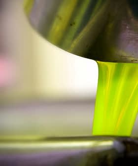Bright green olive oil pouring from a metal container into a bowl. - Olive Oil Times