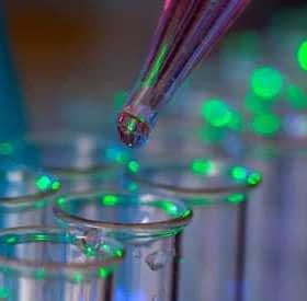 A pipette dropping liquid into a row of clear test tubes illuminated with green light. - Olive Oil Times
