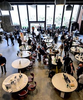 Interior of a spacious event venue featuring round tables and attendees engaged in conversation. - Olive Oil Times
