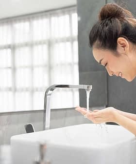 A woman in a white robe washing her hands at a modern sink with flowing water. - Olive Oil Times