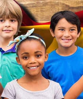 Five children posing together in front of a Spanish flag background, smiling and wearing casual clothing. - Olive Oil Times