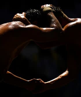 Two wrestlers in a close hold during a match, with their bodies glistening under the light. - Olive Oil Times