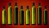 Eight green glass bottles with black caps arranged in a row against a gradient background. - Olive Oil Times
