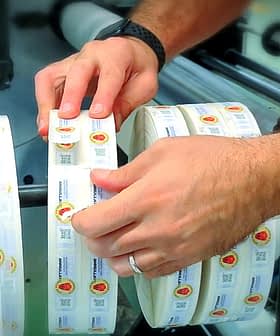 Individual placing labels on a roll of adhesive labels in a manufacturing setting. - Olive Oil Times