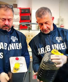 Two men in uniforms holding a metal container and a plastic bottle filled with oil. - Olive Oil Times