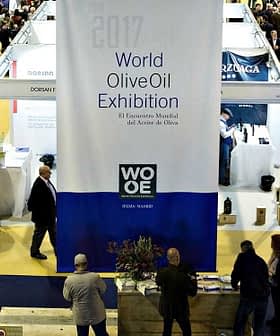 Crowd of attendees at the World Olive Oil Exhibition with a large banner in the center. - Olive Oil Times
