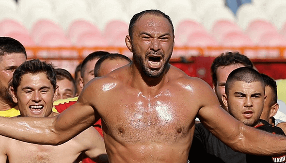 Group of enthusiastic fans celebrating at a sports event with one man prominently shouting. - Olive Oil Times